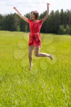 Young girl in a red dress jumping in a field on a sunny day