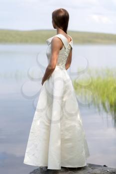 girl in a white dress standing on a rock against the backdrop of the lake, the view from the back