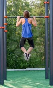 Young athletic girl pulls on the bar, the view from the back.