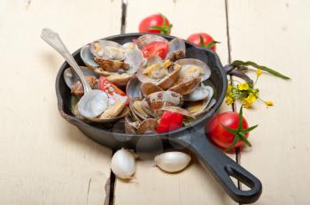 fresh clams stewed on an iron skillet over wite rustic wood table 