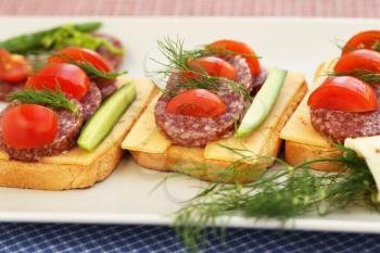 Sandwiches with salami, cheese, cherry tomato and dill on plate.