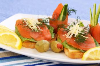 Sandwiches with salmon, cheese, lettuce,  herbs on plate, olives and lemons.