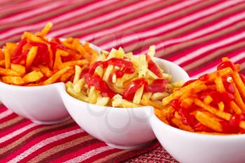 Potato chips and red sauce isolated on colorful tablecloth.
