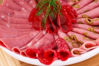 Salami, mortadella and bacon on plate on wooden board.