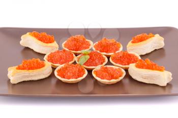 Red caviar in round pastries on brown plate.