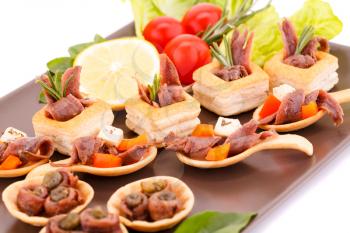 Anchovies in pastries, lemon, tomato, lettuce and basil on brown plate.