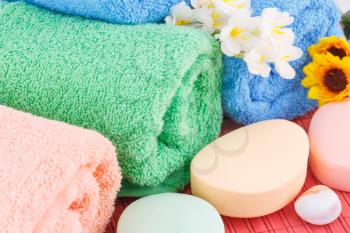 Colorful rolled towels with flowers, soaps and stones closeup picture.