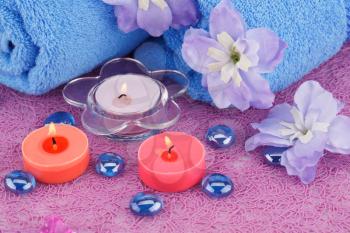 Spa set with towels, candles and flowers on plastic background.