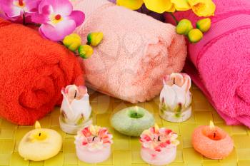 Spa set with towels, candles and flowers on bamboo background.