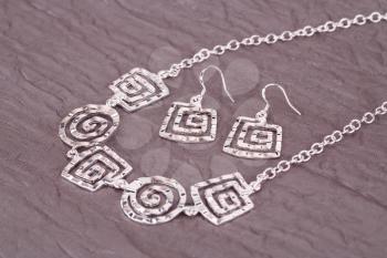 Silver necklace and earrings on fabric background.