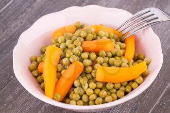 Peas and carrots in bowl isolated on wooden background.