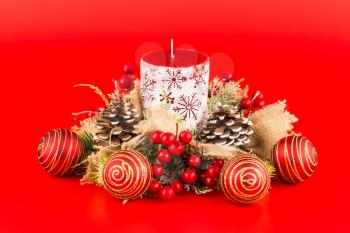 Christmas decoration with candle, balls, holly berry and cones on red background.