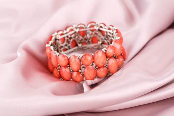 Stylish bracelet with stones on fabric background.