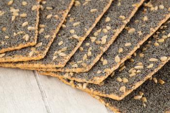 Pile of crackers with poppy and sunflower seeds on gray wooden background.