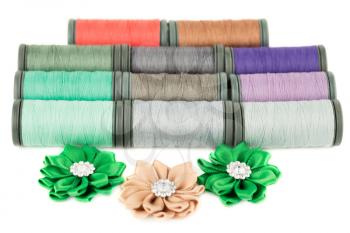Colorful cotton thread reels and fabric flowers isolated on white background.