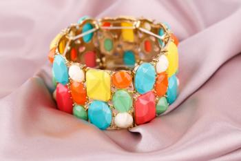 Stylish bracelet with colorful stones on fabric background.