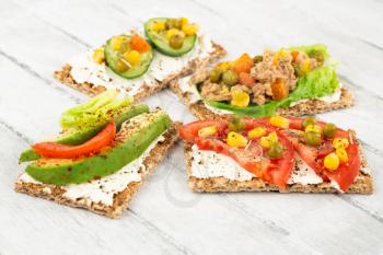 Sandwiches with crackers, cheese, tuna fish and vegetables on gray wooden background.