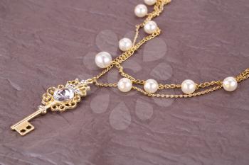 Stylish necklace with pearls and key on fabric background.