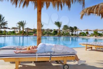 Senior woman lie on chaise longue , near water pool in resort-spa hotel