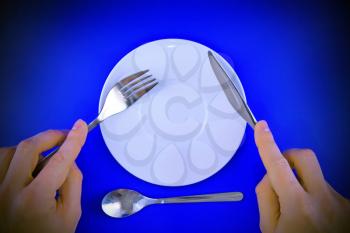 Table serving-knife, fork in hands on blue background.