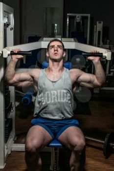 young bodybuilder doing shoulder press on machine