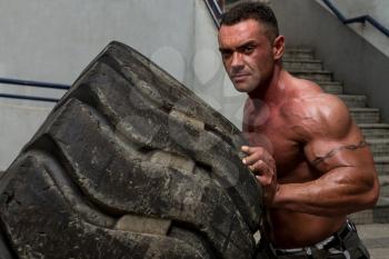 A muscular man participating in a cross fit workout by doing a tire flip