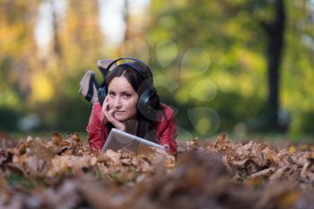 Young Woman Lying Outside And Listening To Headphones
