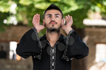 Young Muslim Man Making Traditional Prayer To God While Wearing A Traditional Cap Dishdasha