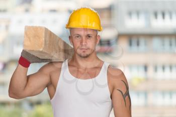 Smiling Carpenter Carrying A Large Wood Plank On His Shoulder