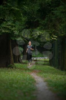 Young Woman Running In Wooded Forest Area - Training And Exercising For Trail Run Marathon Endurance - Fitness Healthy Lifestyle Concept