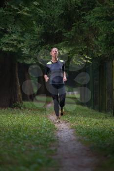 Young Woman Running In Wooded Forest Area - Training And Exercising For Trail Run Marathon Endurance - Fitness Healthy Lifestyle Concept