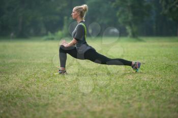 Young Woman Stretching Before Running In Wooded Forest Area - Training And Exercising For Trail Run Marathon Endurance - Fitness Healthy Lifestyle Concept