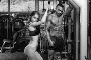 Strong Young Couple Working Out On Machine For Triceps In The Gym With Exercise Equipment
