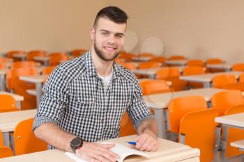 Portrait Of Young Male College Student With Book Sitting In Classroom Alone