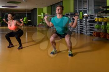 Young Couple Working Out Legs With Barbell In Fitness Center - Squat