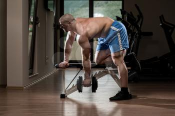 Muscular Man Doing Heavy Weight Exercise For Back With Dumbbell In Gym