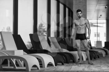 Young Muscular Man Flexing Muscles By Swimming Pool And Sun Loungers