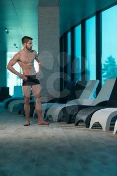 Young Muscular Man Flexing Muscles By Swimming Pool And Sun Loungers