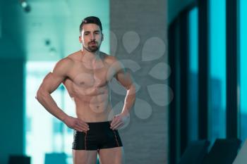 Young Muscular Man Flexing Muscles By Swimming Pool And Sun Loungers