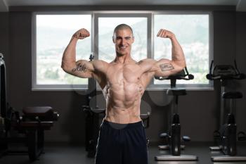 Young Man Standing Strong In The Gym And Flexing Muscles - Muscular Athletic Bodybuilder Fitness Model Posing After Exercises