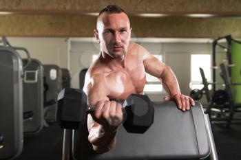 Muscular Young Man Doing Heavy Weight Exercise For Biceps With Dumbbells In Modern Fitness Center Gym