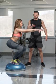 Personal Trainer Showing Young Woman How To Train On Bosu Balance Ball In A Gym