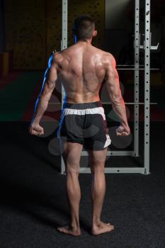 Young Man Standing Strong In The Gym And Flexing Side Triceps Pose - Muscular Athletic Bodybuilder Fitness Model Posing Exercises