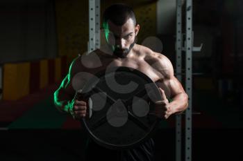 Portrait Of A Physically Young Man Holding Weights In Hand In A Dark Gym