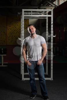 Smiling Young Man In Jeans Standing In A Dark Gym