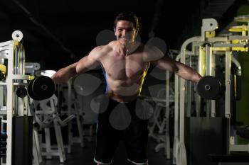 Young Man Working Out Shoulders In A Dark Gym - Bodybuilder Doing Heavy Weight Exercise For Shoulder