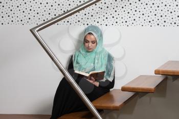 Muslim Woman Reading Koran Or Quran Wearing Traditional Dress At The Mosque