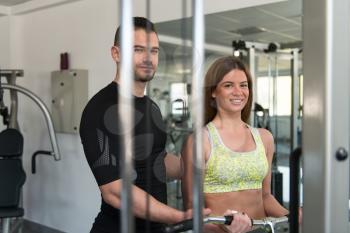 Personal Trainer Showing Young Woman How To Train Biceps On Machine In The Gym