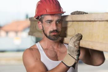 Smiling Carpenter Carrying A Large Wood Plank On His Shoulder