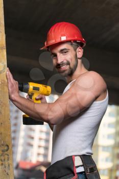 Successful Male Architect At A Building Site Trying To Drill A Large Wood Plank